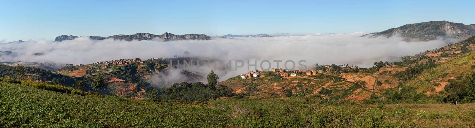 Fog over valley with small village on sunny morning in region near Alakamisy Ambohimaha, Madagascar.