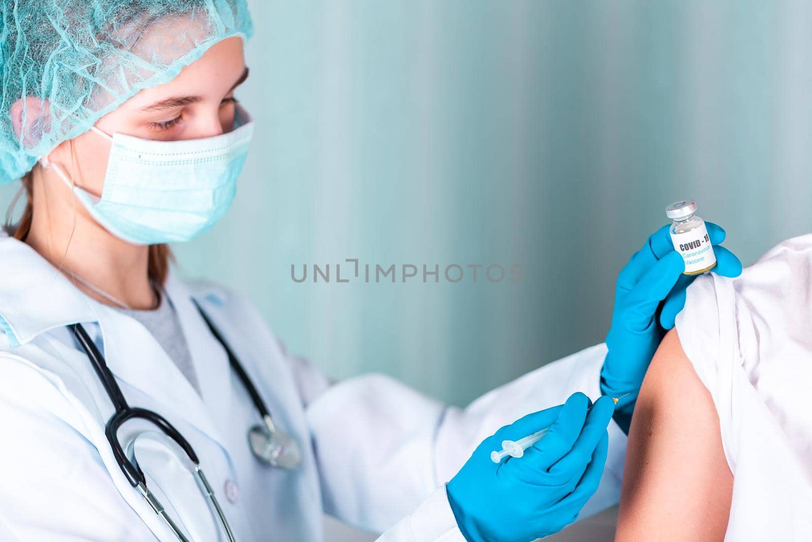 Woman doctor or nurse in uniform and gloves wearing face mask protective in lab, making an injecion holding vaccine bottle with COVID-19 Coronovirus vaccine label