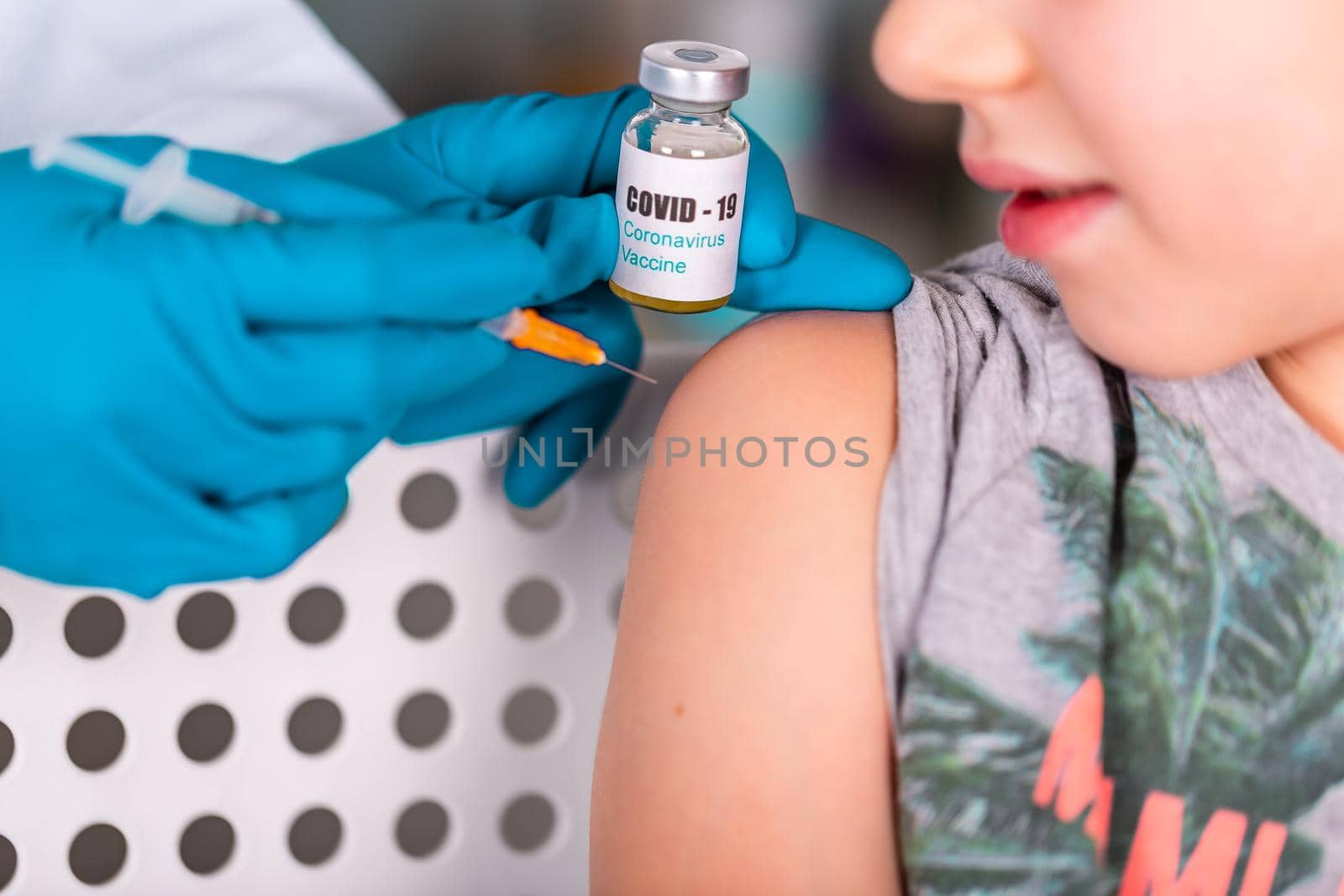 Woman doctor or nurse in uniform and gloves wearing face mask protective in lab, making an injecion to a kid holding vaccine bottle with COVID-19 Coronovirus vaccine label