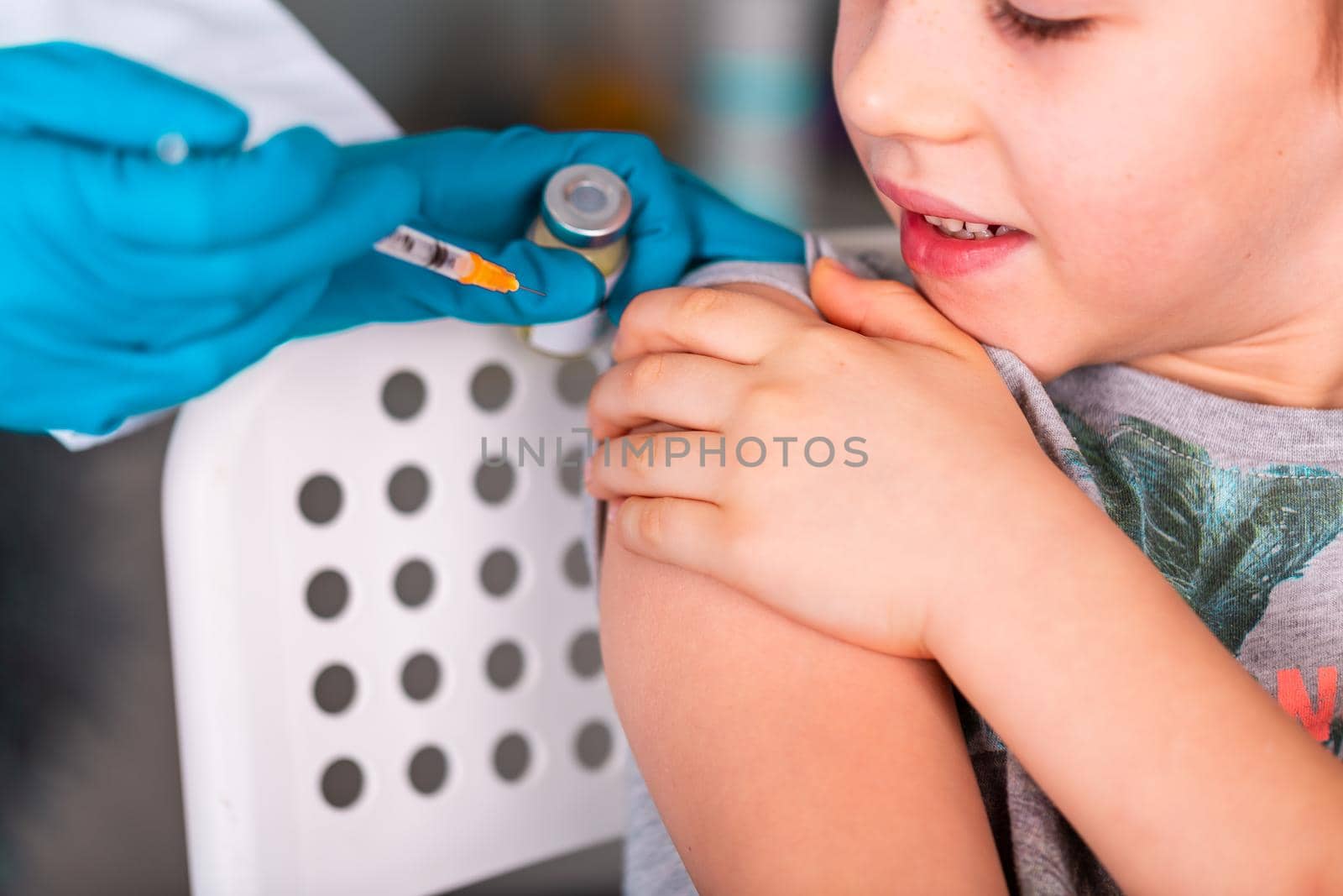 Woman doctor or nurse in uniform and gloves wearing face mask protective in lab, making an injecion to a kid holding vaccine bottle with COVID-19 Coronovirus vaccine label