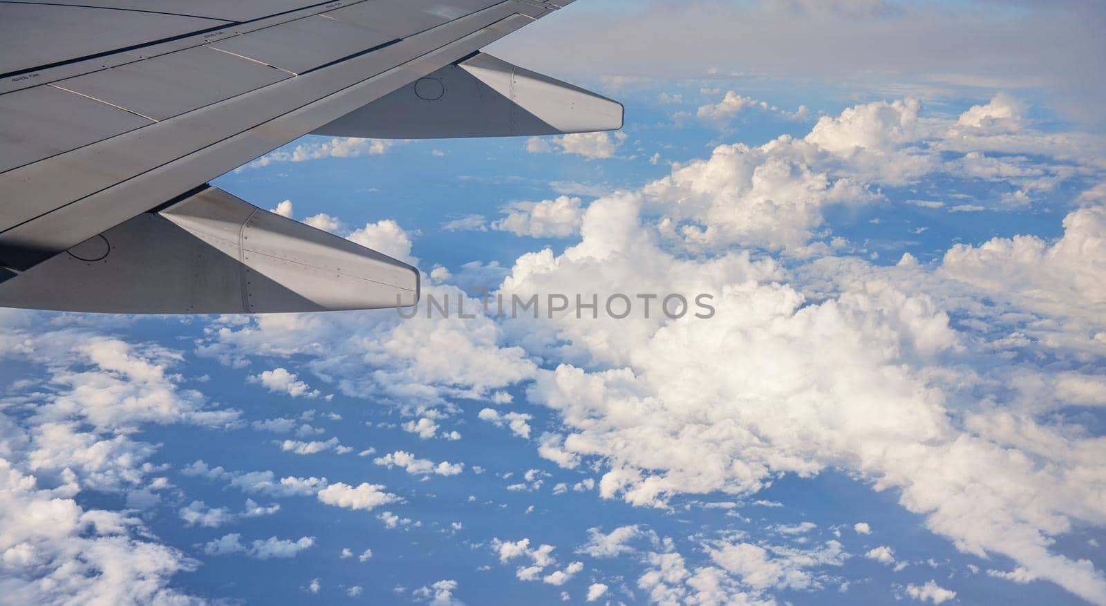 View from passenger window of commercial airplane, clouds on blue sky visible under aircraft wing.