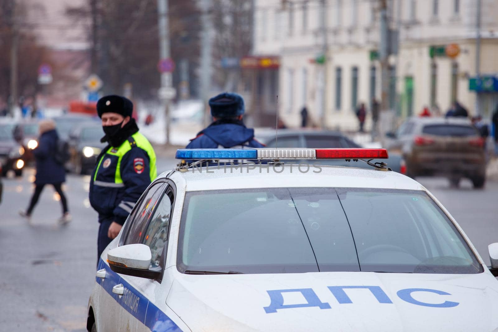 Tula, Russia - January 23, 2021: Russian road police officers standing near patrol car and dirty snow on winter city road - close-up with selective focus on roof lamp. Letters DPS mean Traffic Patrol Police