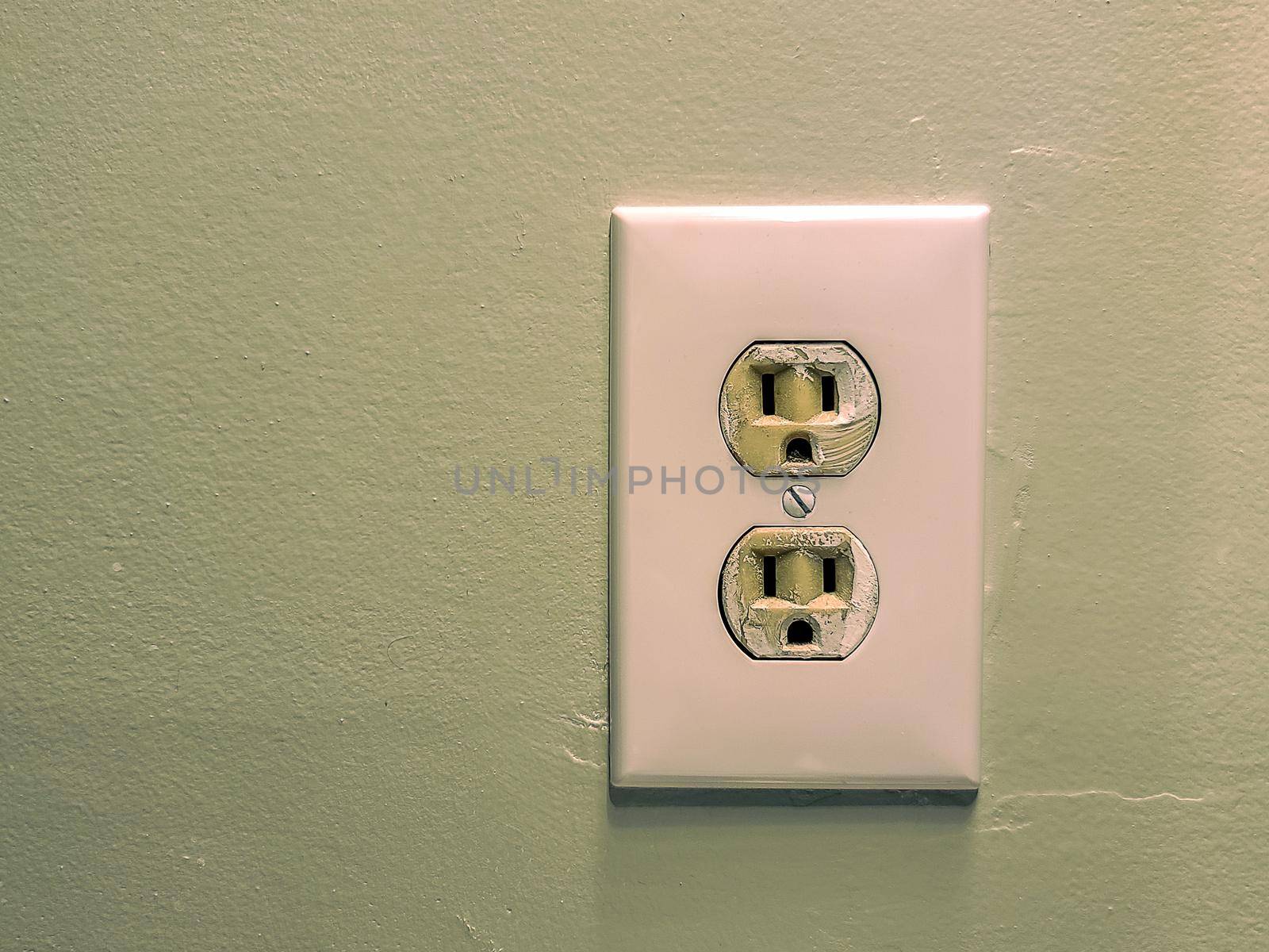 White electrical wall outlet with two sockets mounted on a green painted wall.