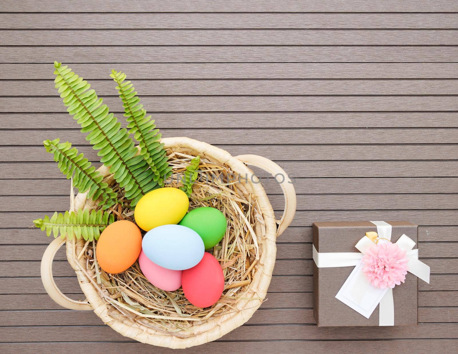 Colorful easter eggs in the basket and gift box on wood background with space