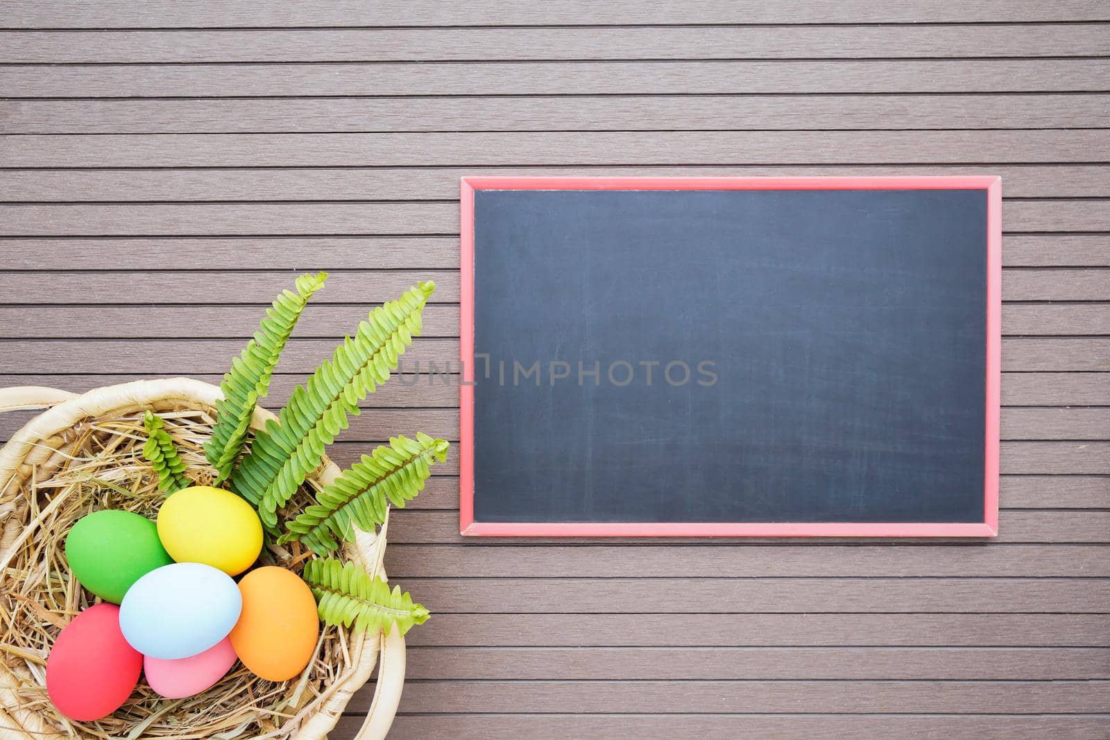 Colorful easter eggs in the basket and blackboard on wood background with space