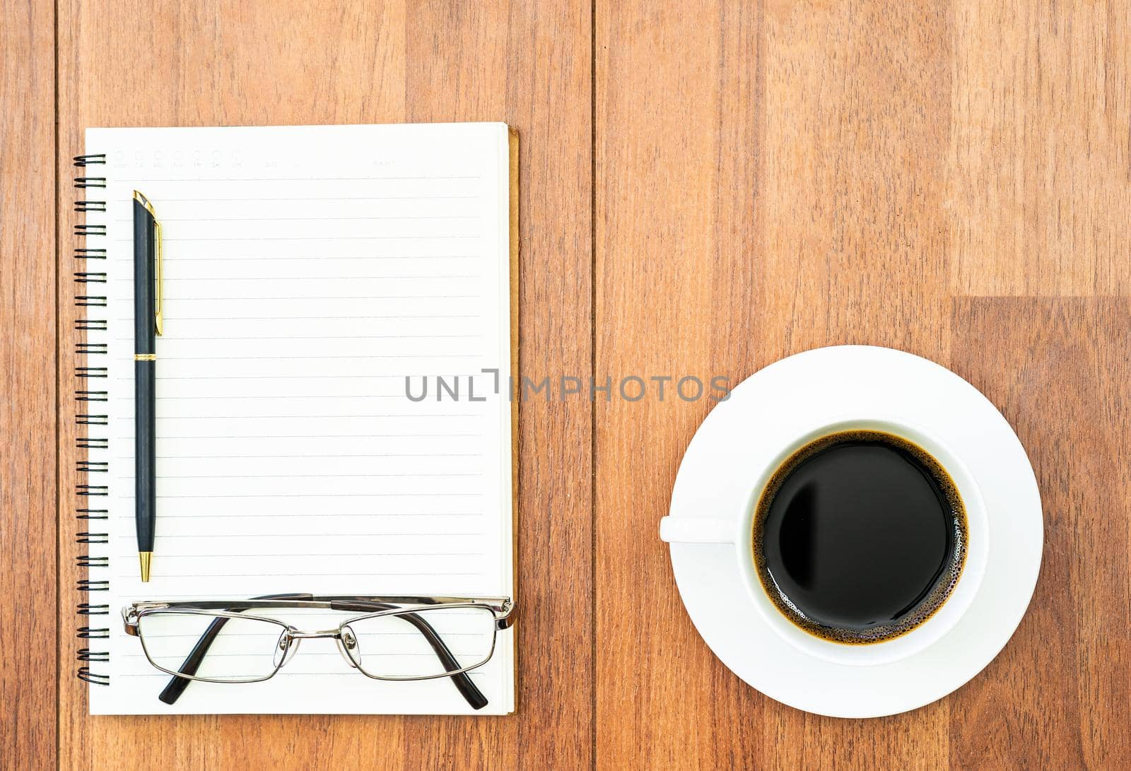 Top view eyeglasse and pen on notepad and coffee cup on wood deck