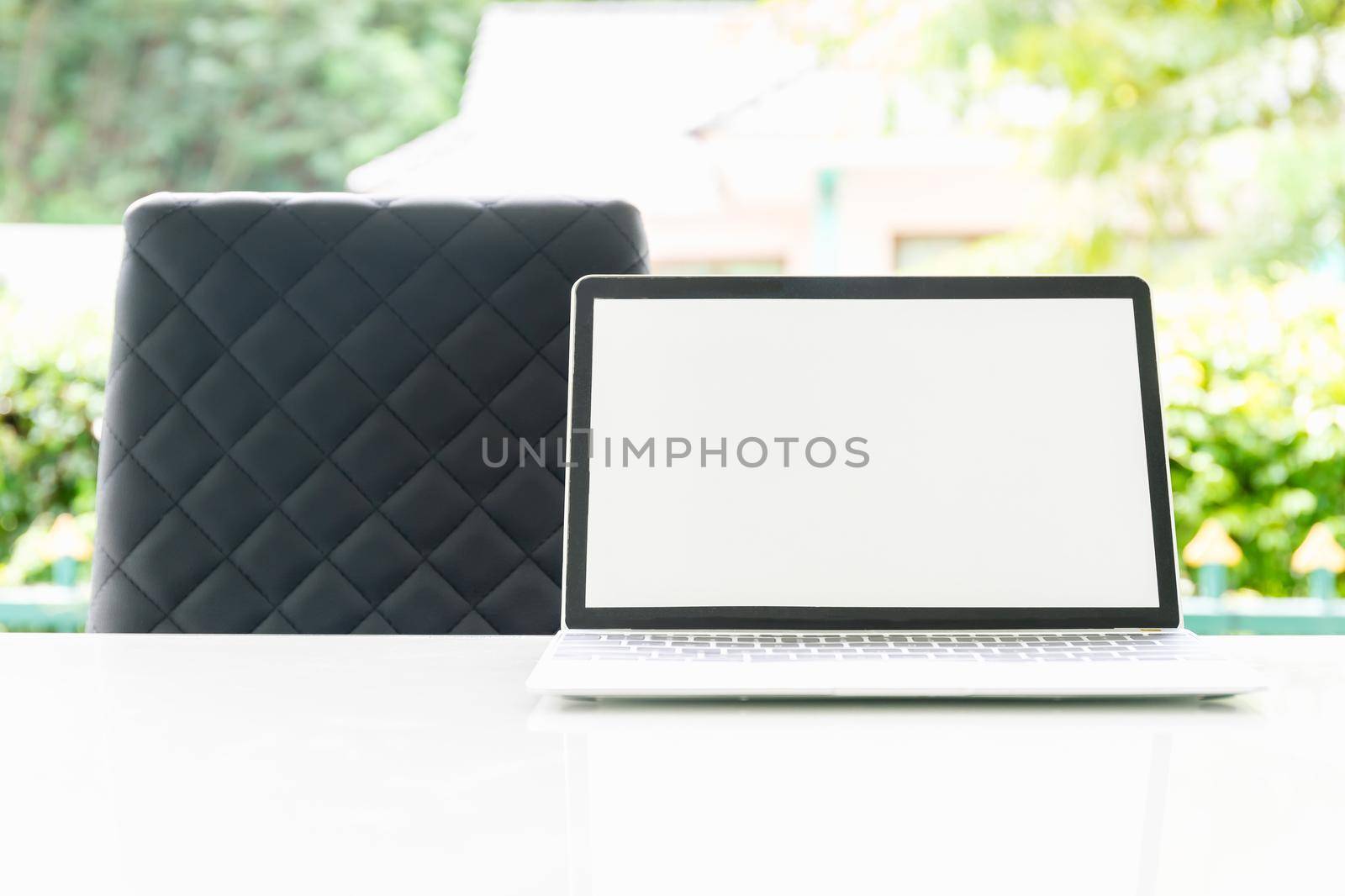 Laptop computer and cup of coffee on the table outdoor in morning with blurred green plant background