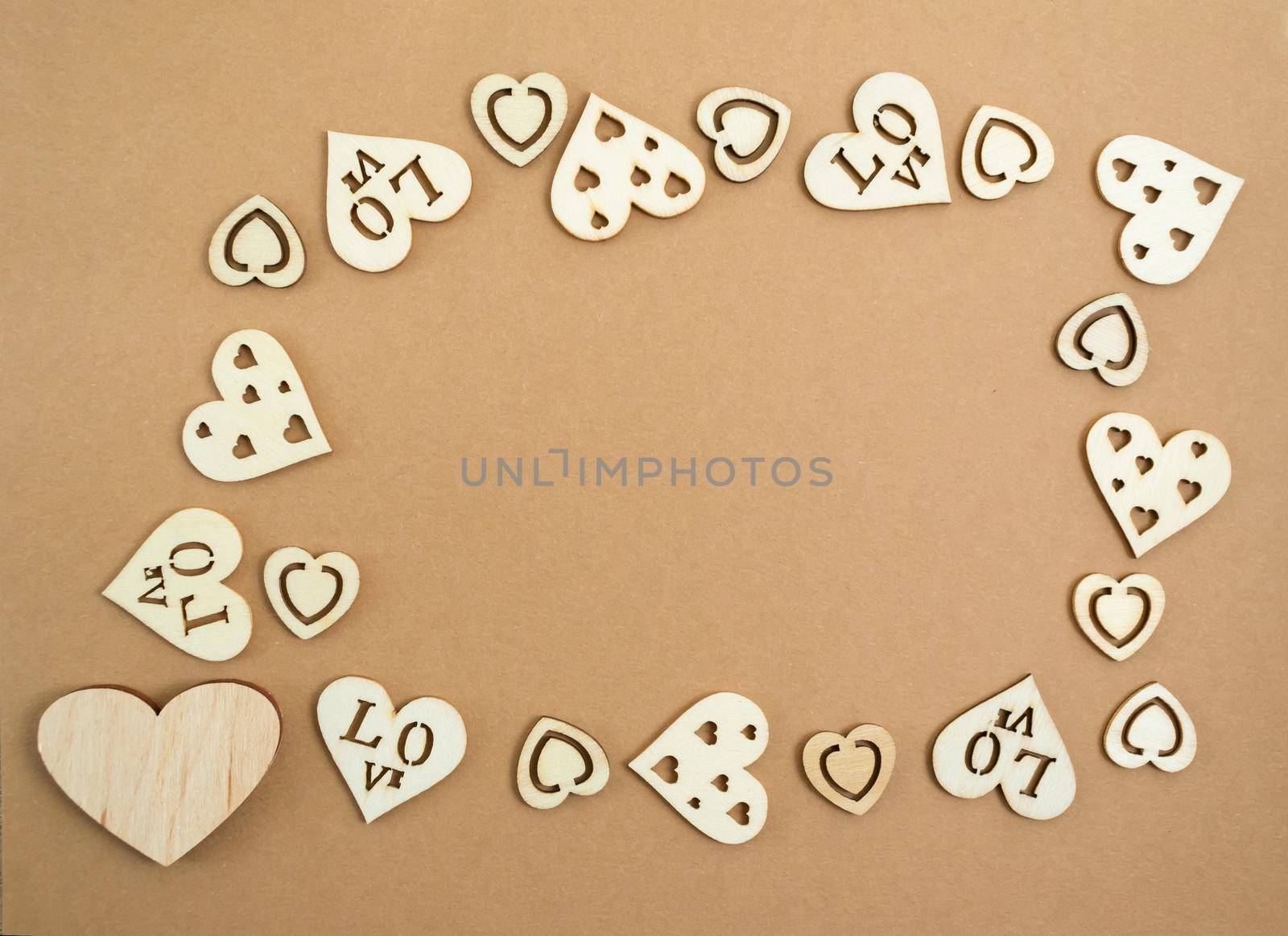 Wooden hearts on a pastel craft paper background in the form of a frame. Abstract background with wood cut shapes. Sainte Valentine. Copy space.