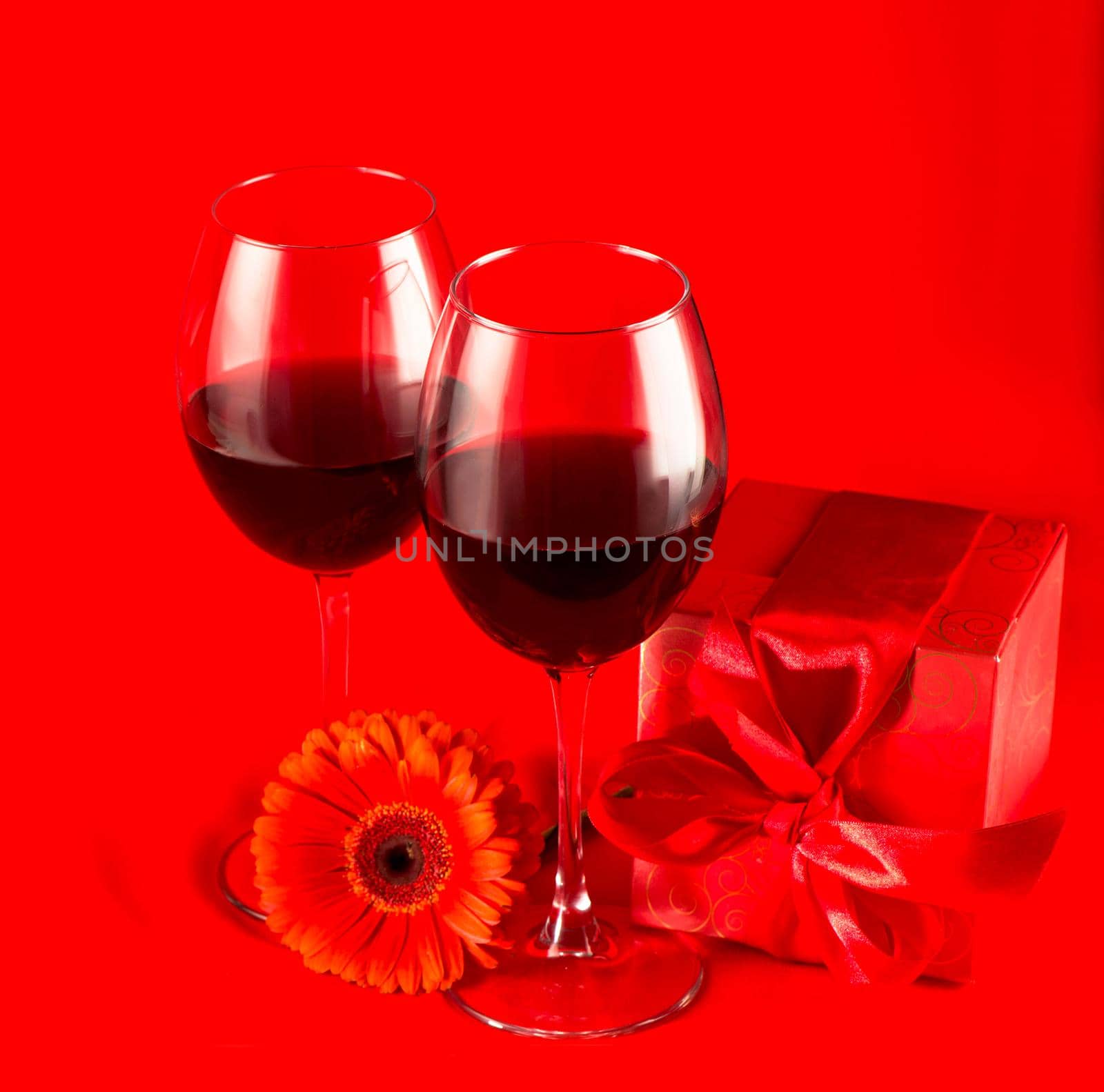 Valentine's Day. Gift box, flowers, glasses with wine and candy in the form of a heart on a red background by aprilphoto
