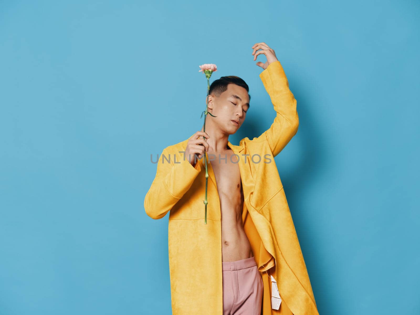 Asian guy with a flower in his hands and a yellow coat blue background. High quality photo