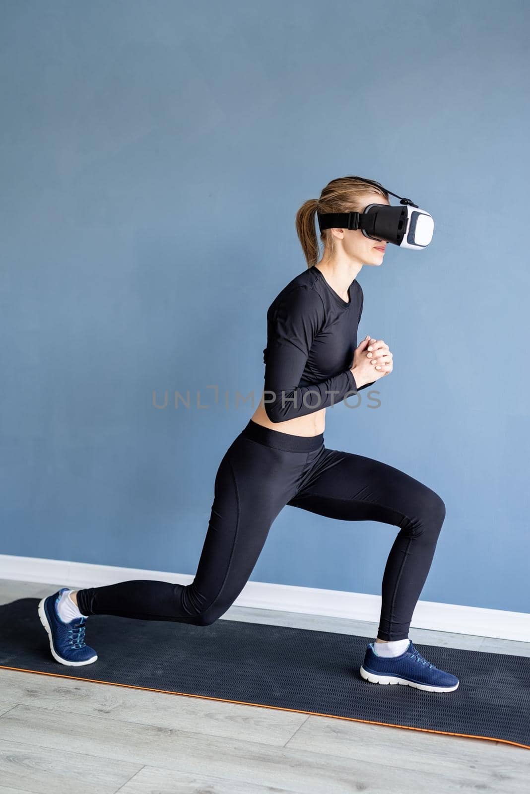 Young blonde woman wearing virtual reality glasses doing front lunge by Desperada