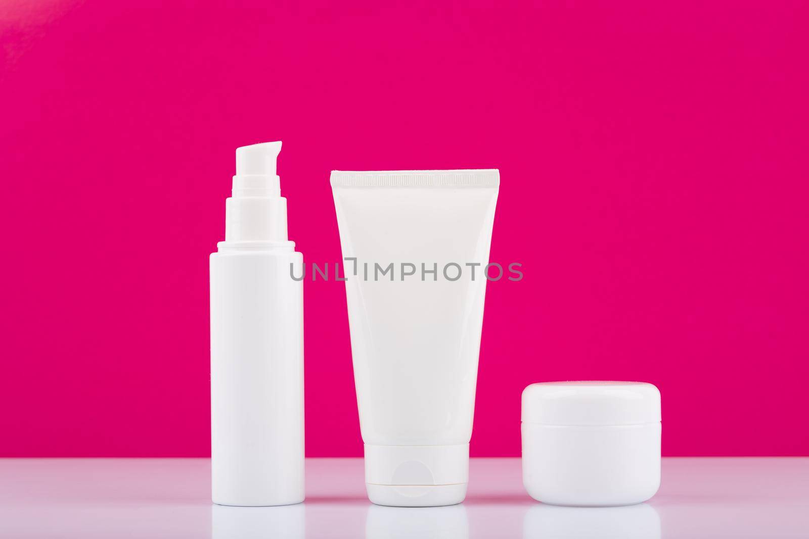 Minimalistic still life with three white glossy cream jars on white table against pink background. Concept of daily skin care. High quality photo