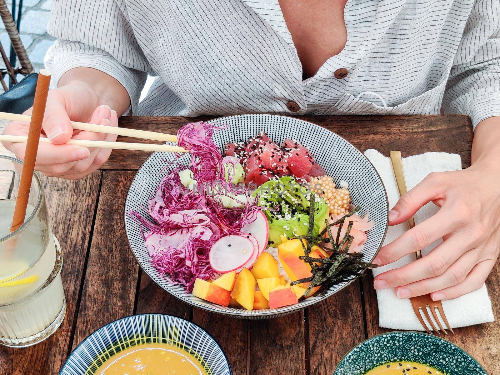 Woman eating tasty colorful healthy natural organic vegetarian Hawaiian poke bowl using asian chopsticks on rustic wooden table. Healthy natural organic eating concept.