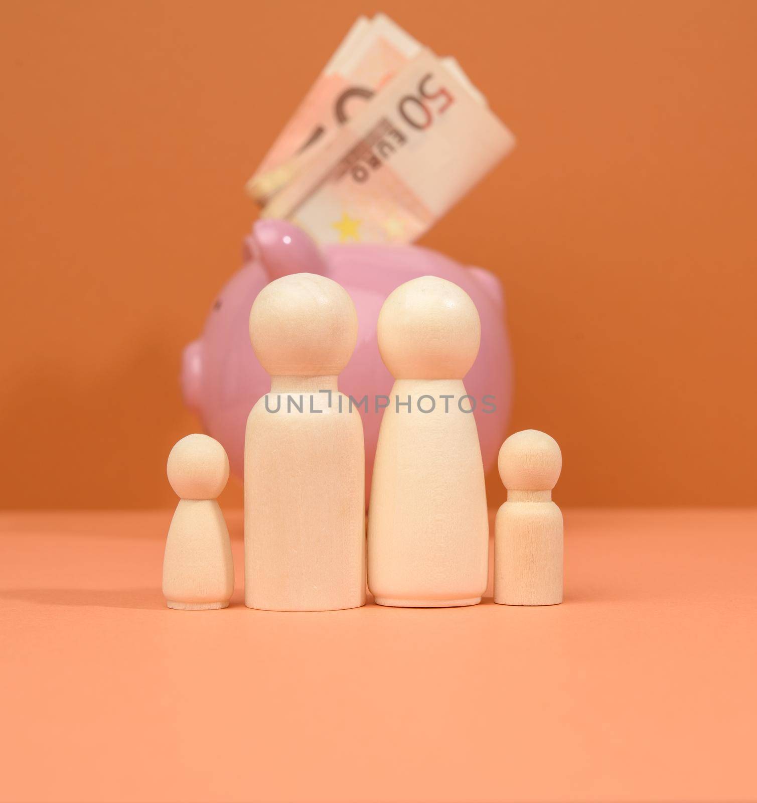 family of wooden figures on the background of a pink piggy bank, the concept of investment and savings