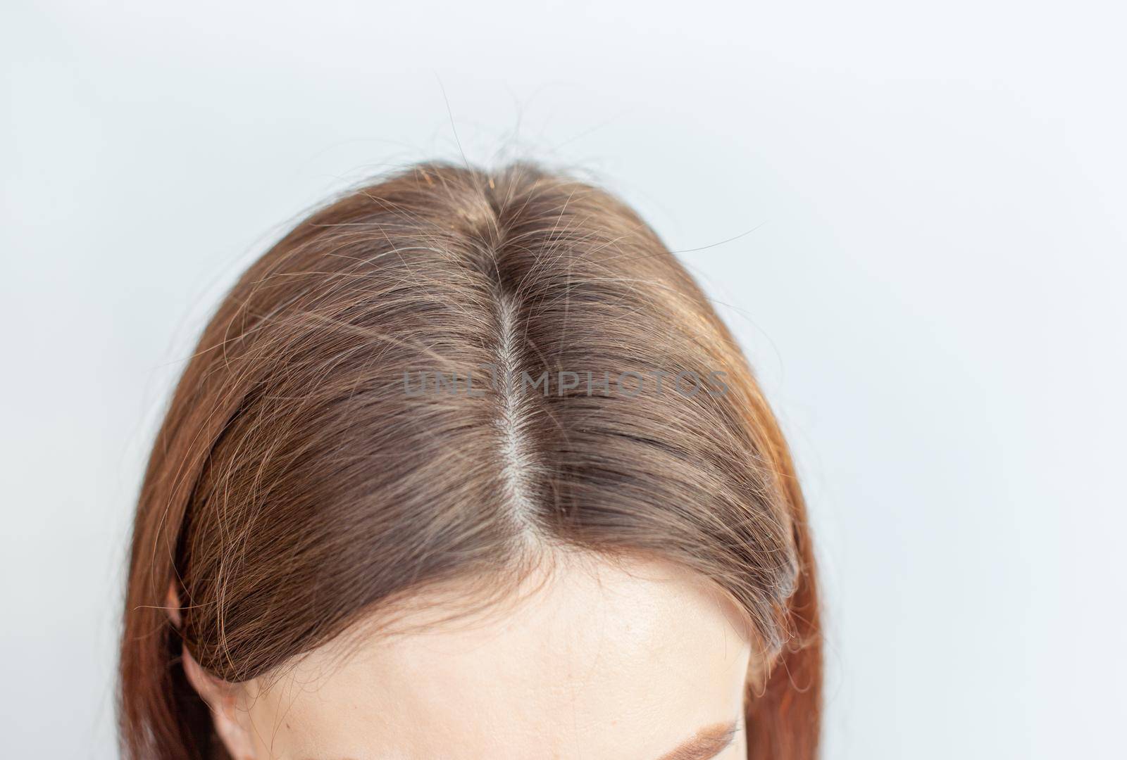 A woman's head with a parting of gray hair that has grown roots due to quarantine. Brown hair on a woman's head close-up.