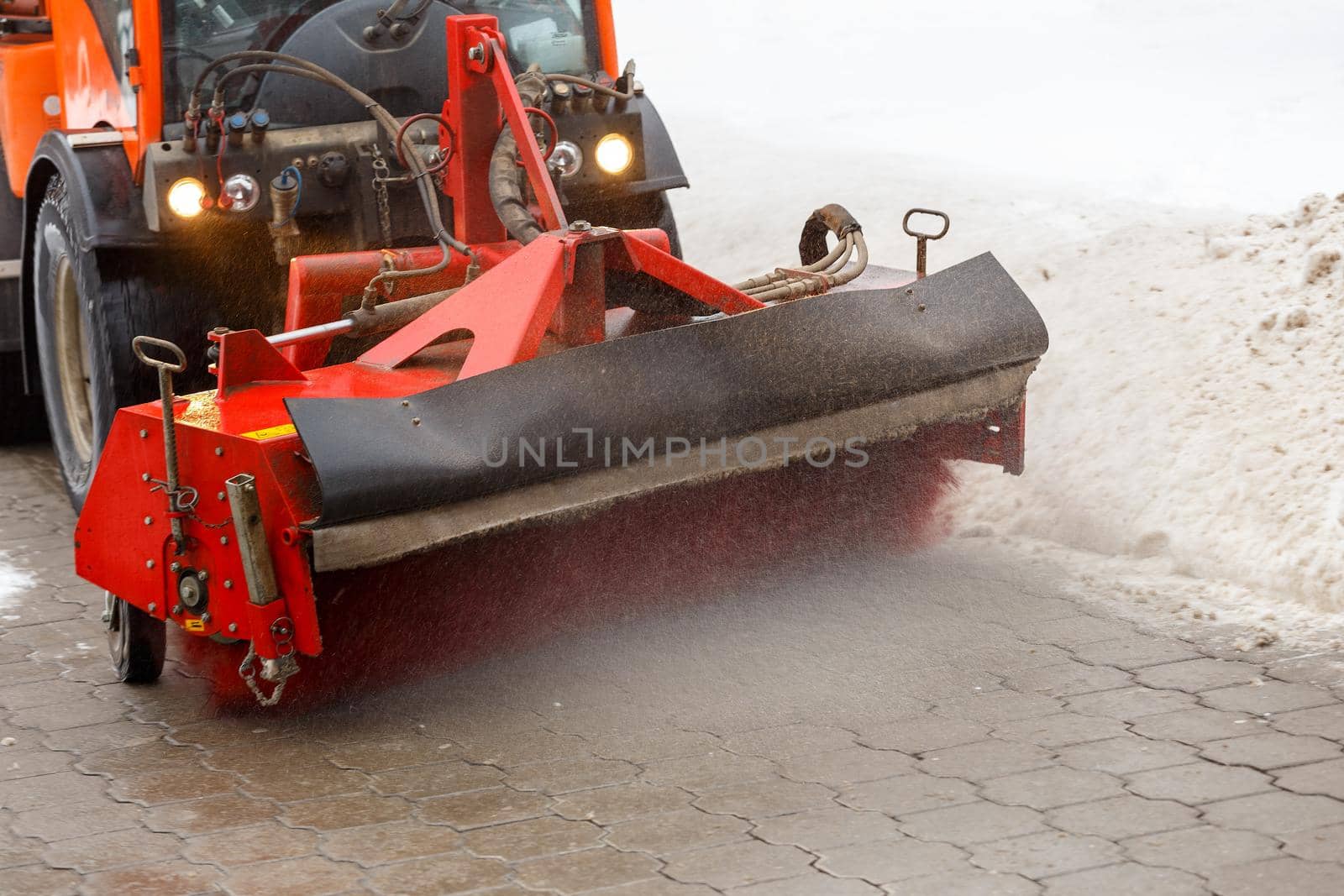 Snow cleaning process at winter city. Snow removal tractor clearing snow from pavement with special round spinning brush.