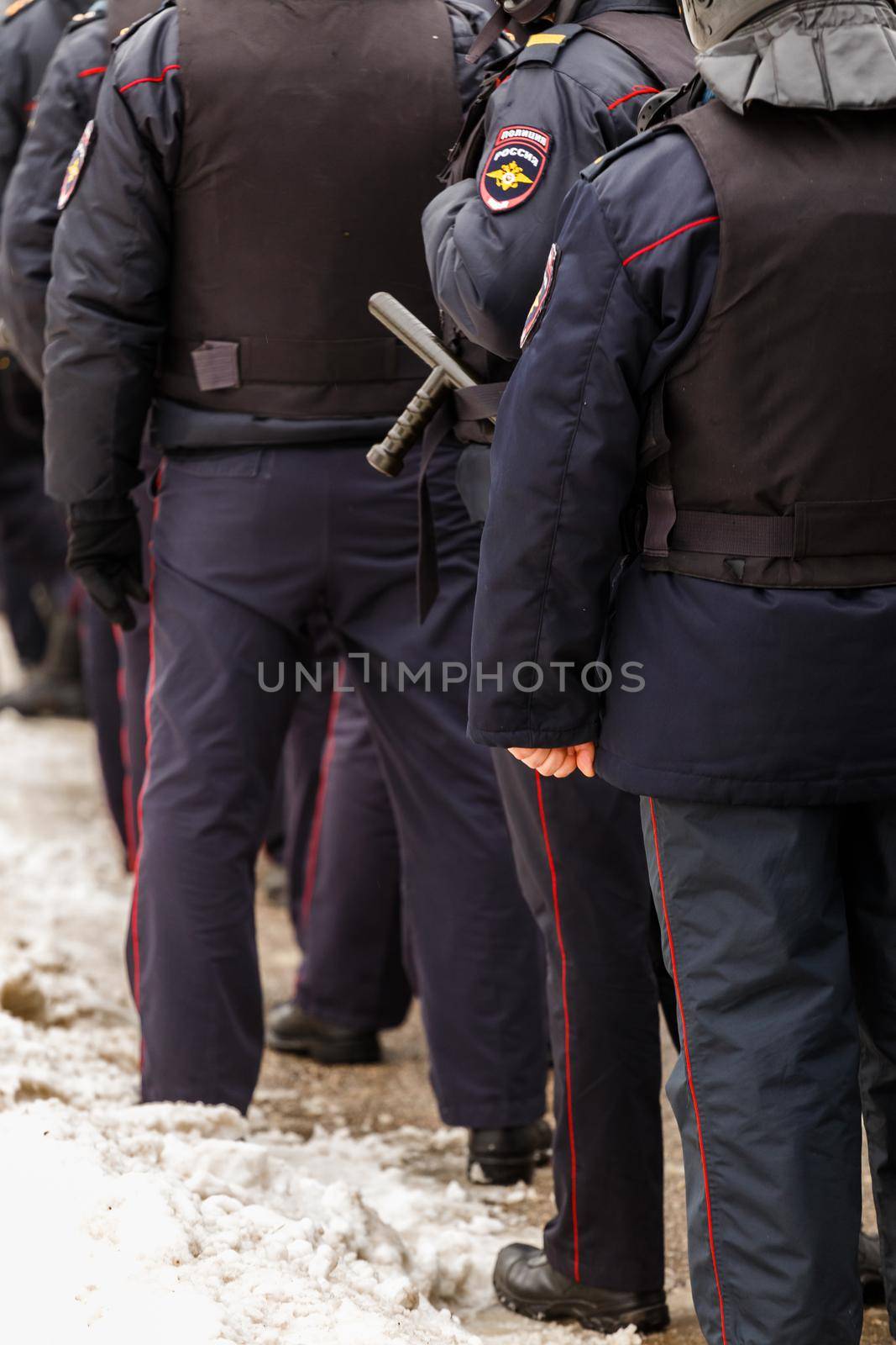 Tula, Russia - January 23, 2021: Crowd of police officers in black uniform with bulletproof vests and pistols - view from back. by z1b