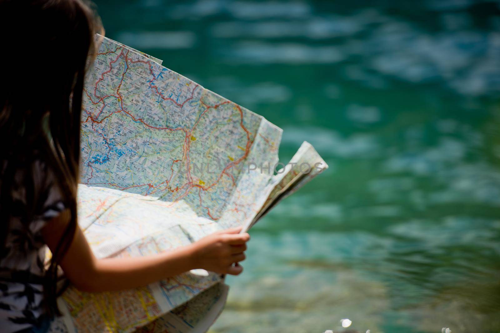 A little sweet girl sits on the shore of the Alpine lake Plansee and looks at the map. Plansee lake, Austria. Close-up.