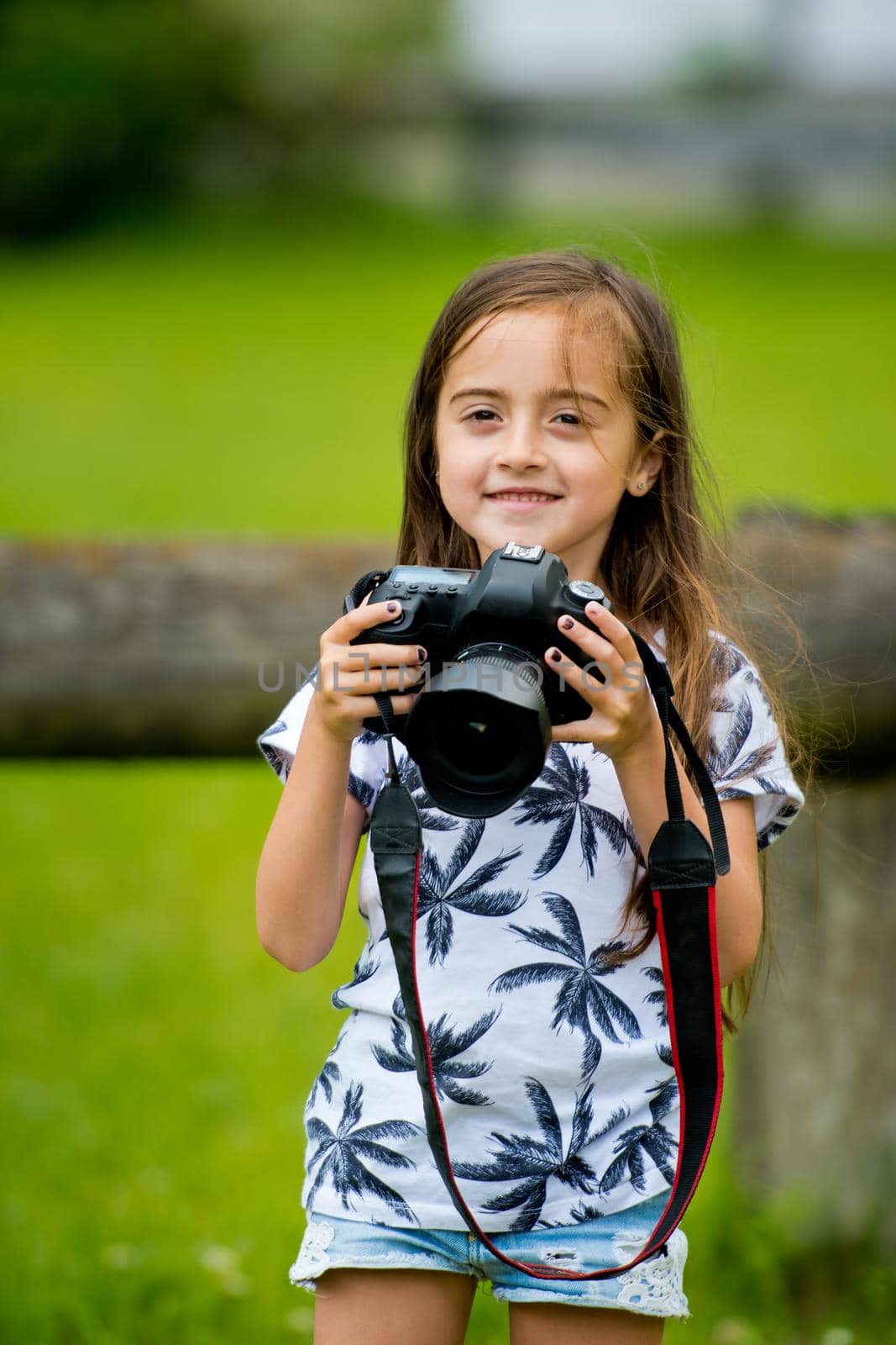 A cute little brunette girl is holding a camera.