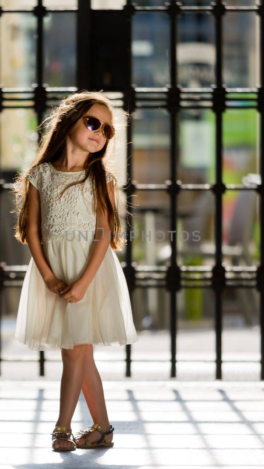 A little sweet girl in a white dress and wearing sunglasses.