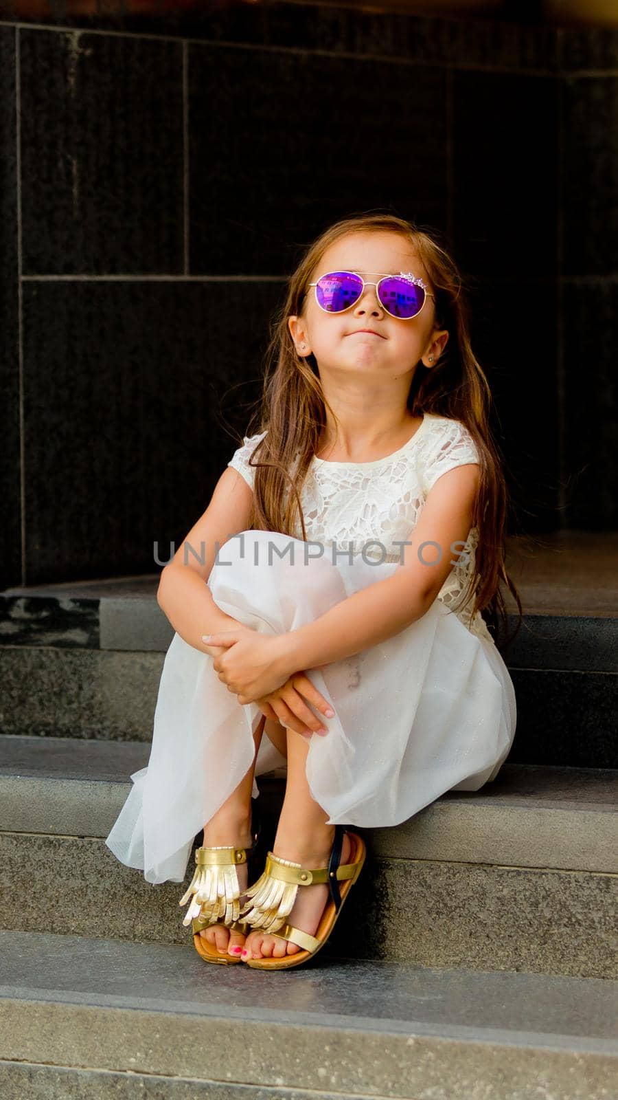 Portrait of a little girl in a white dress in sunglasses.