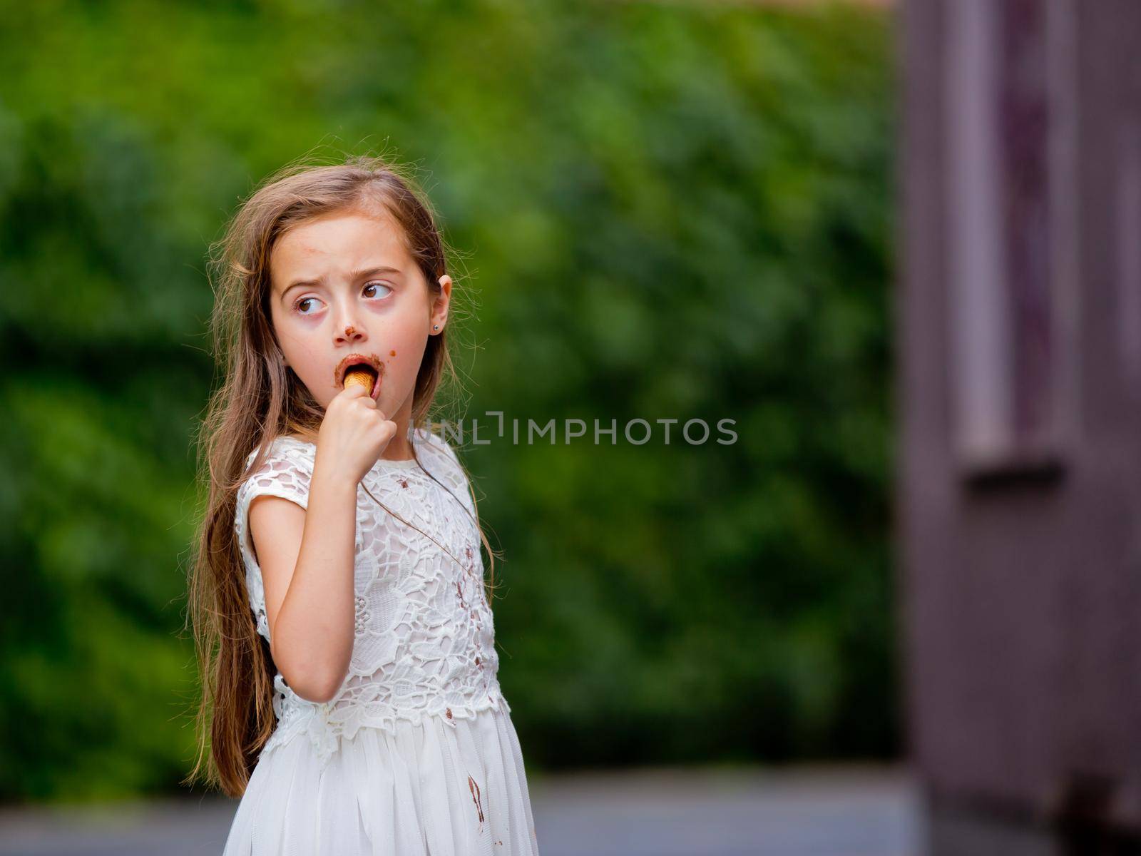 A little girl in a white dress is eating ice cream.