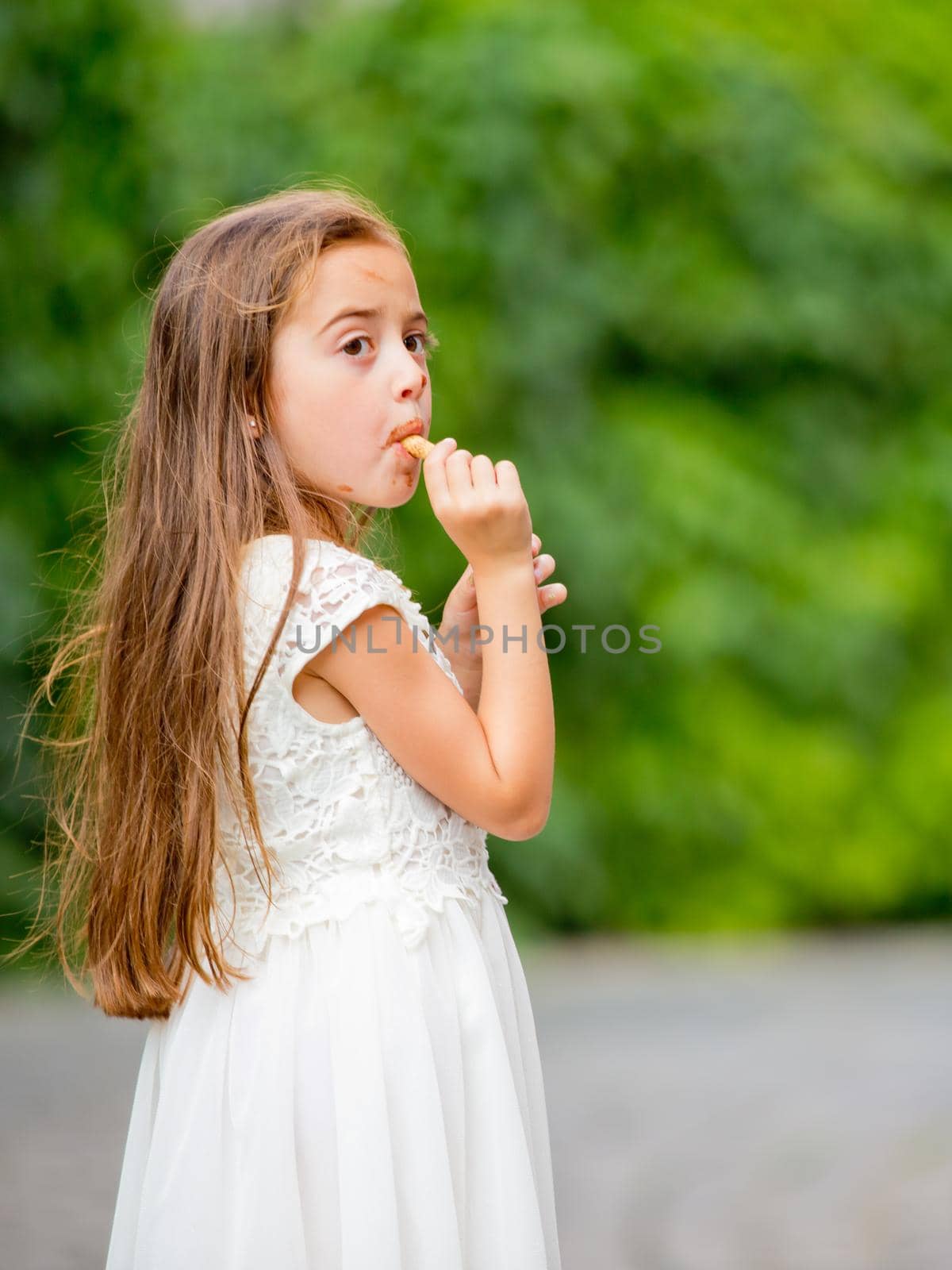 A little girl in a white dress is eating ice cream.