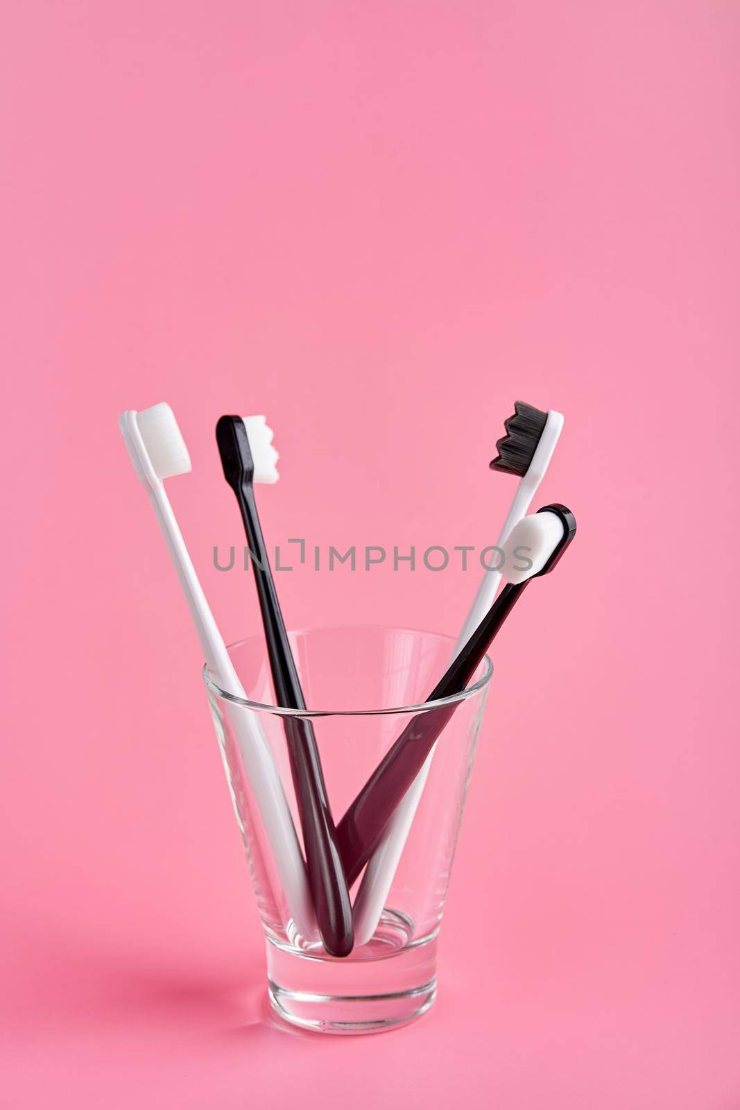 Fashionable toothbrush with soft bristles. Popular toothbrushes. Hygiene trends. Kit of toothbrushes in glass on pink background by Try_my_best