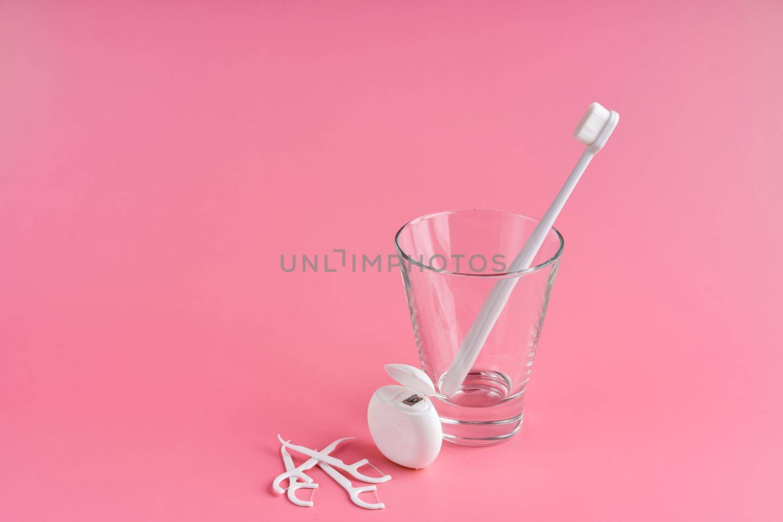 Fashionable toothbrush with soft bristles. Popular toothbrushes. Hygiene trends. Oral hygiene kit. Toothbrushes in glass, floss thread and toothpicks on a pink background.