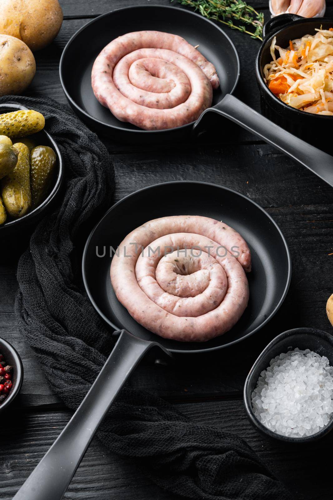 Raw meat sausage set in cast iron frying pan, on black wooden table background
