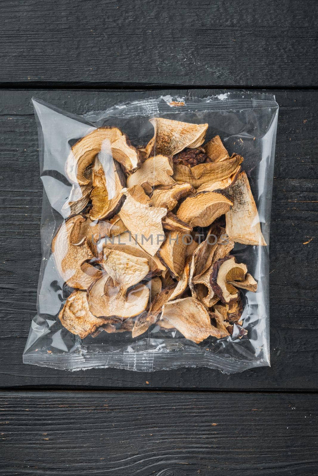 Mix of chopped wild dried mushrooms set, on black wooden table background, in plastic pack, top view flat lay