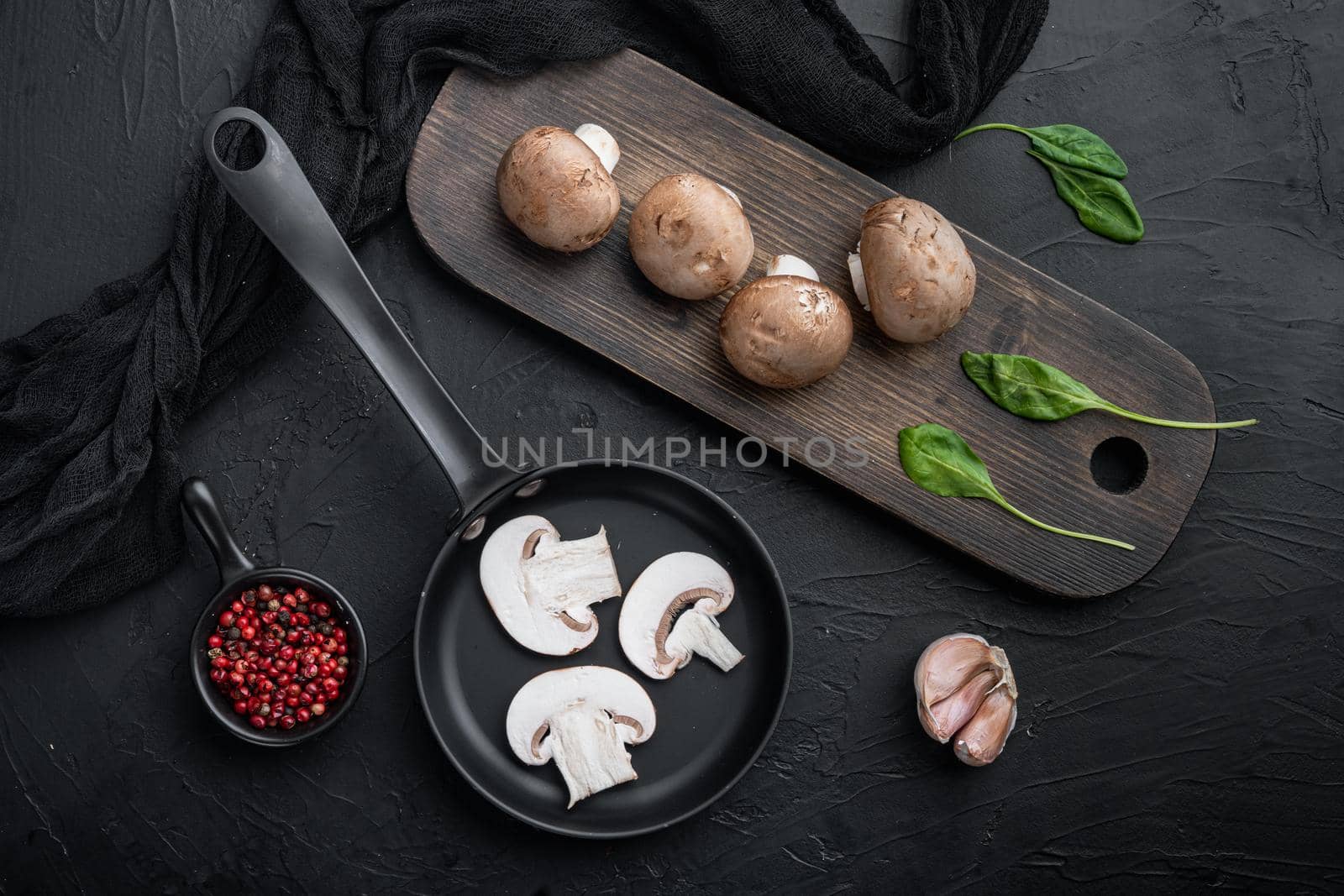Brown champignons mushroom set in cast iron frying pan, on black background, top view flat lay