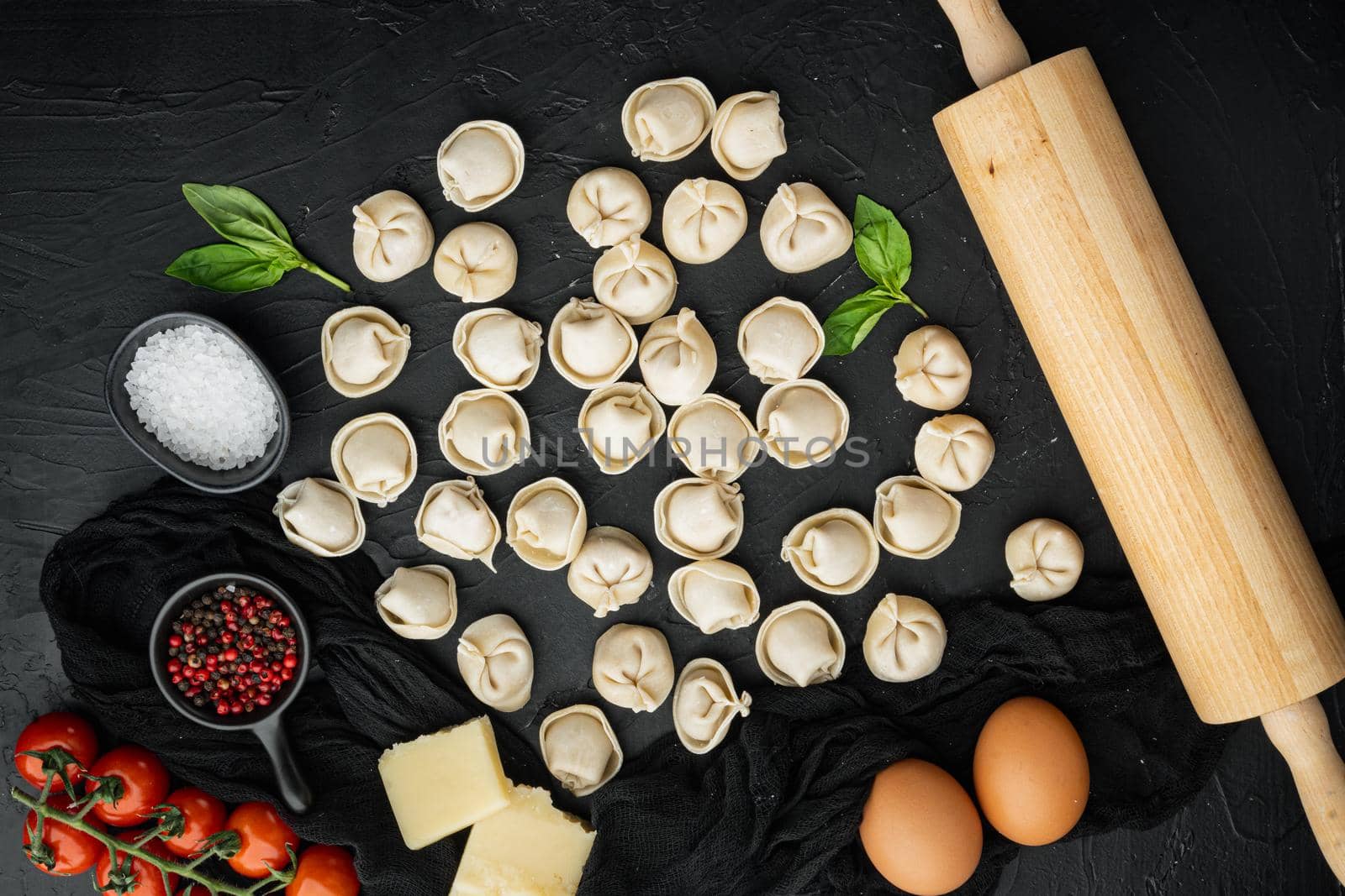 Tasty raw tortellini with flour and basil set, on black background, top view flat lay