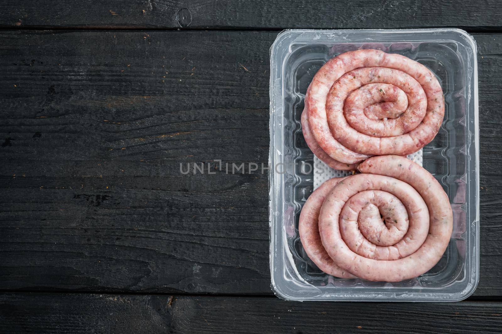 Raw meat sausage set, on black wooden table background, in plastic pack, top view flat lay , with space for text copyspace
