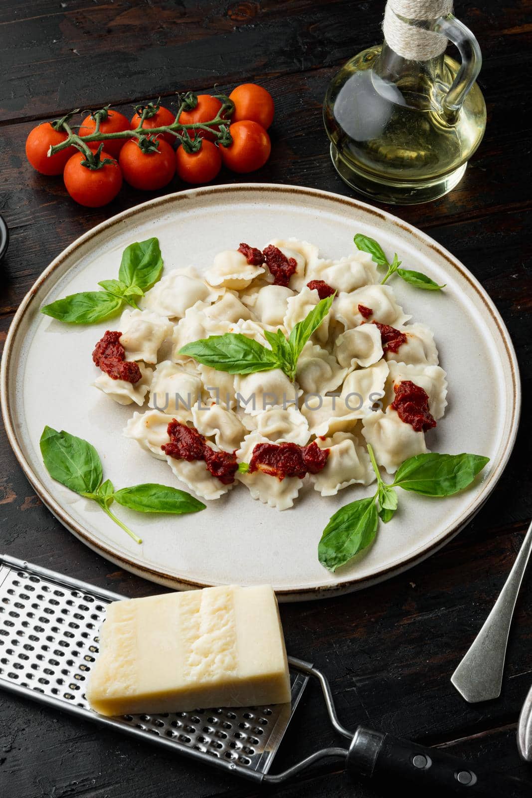 Appetizing ravioli with tomato sauce, cheese and basil set with basil parmesan and tomatoe on white plate on old dark wooden table background