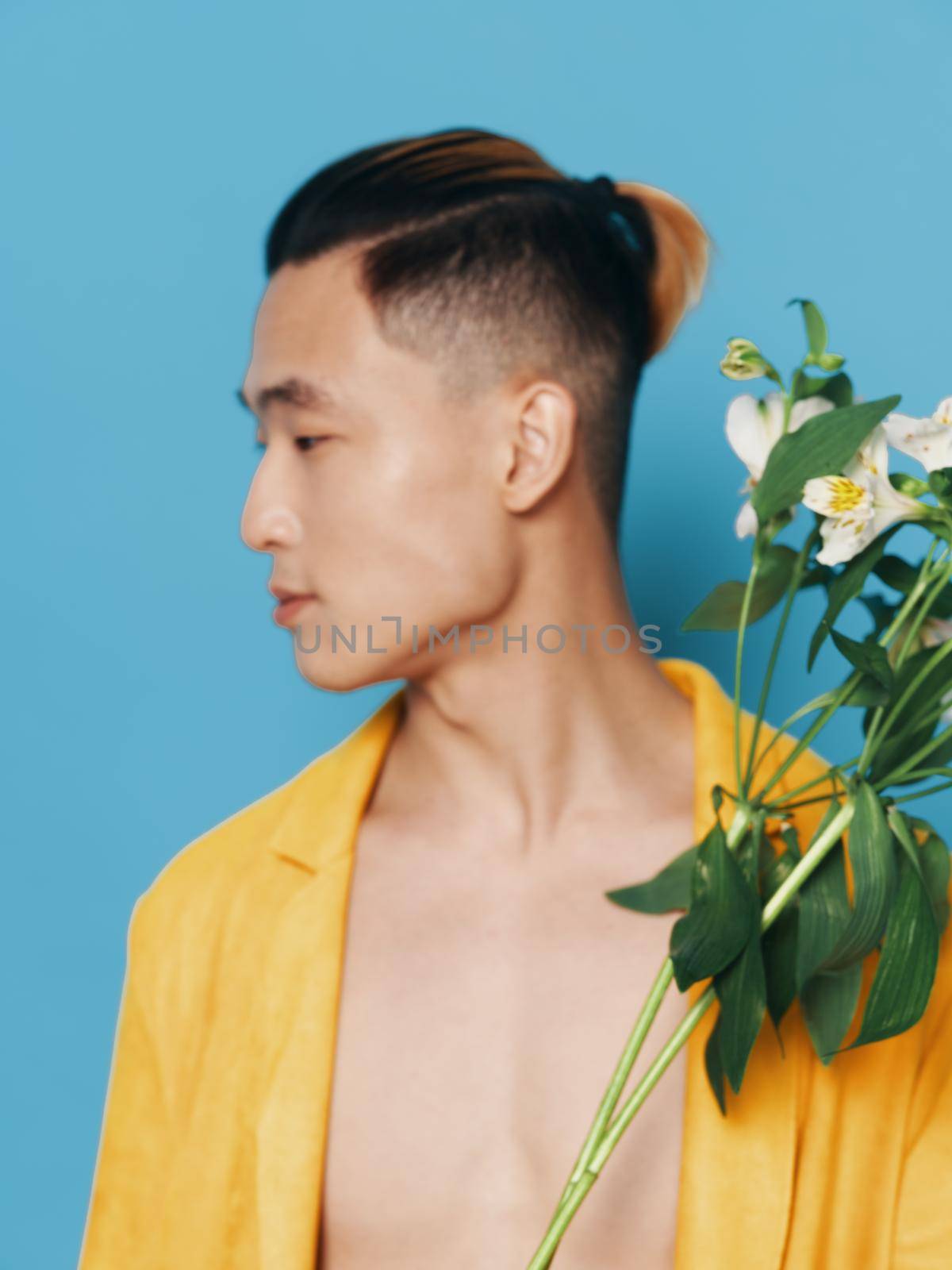 Cute Korean man in a yellow coat with a bouquet of flowers on a blue background model. High quality photo