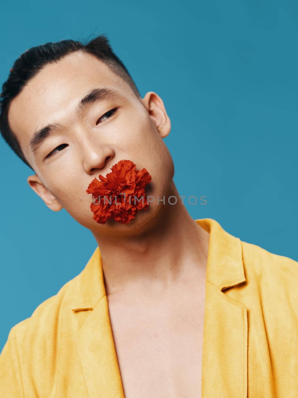 An Asian guy with a flower in his mouth tilted his head to the side against a blue background by SHOTPRIME