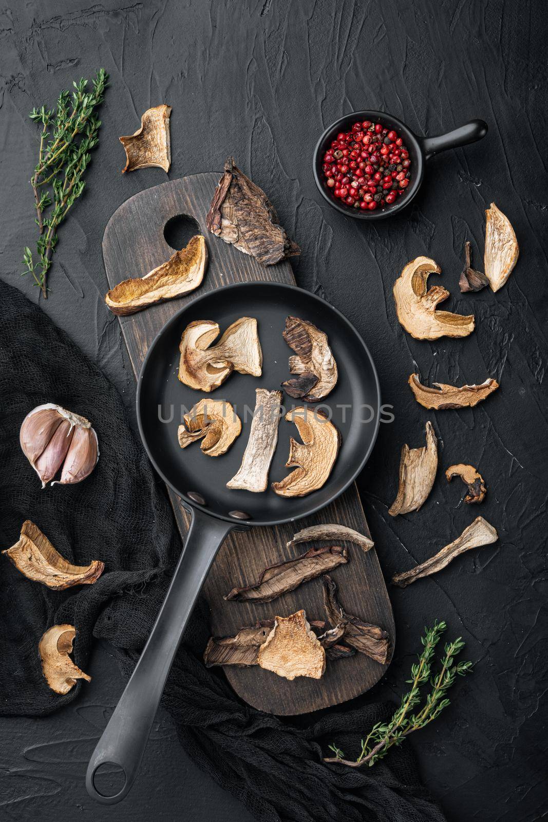 Dried wild mushrooms set in cast iron frying pan, on black background, top view flat lay
