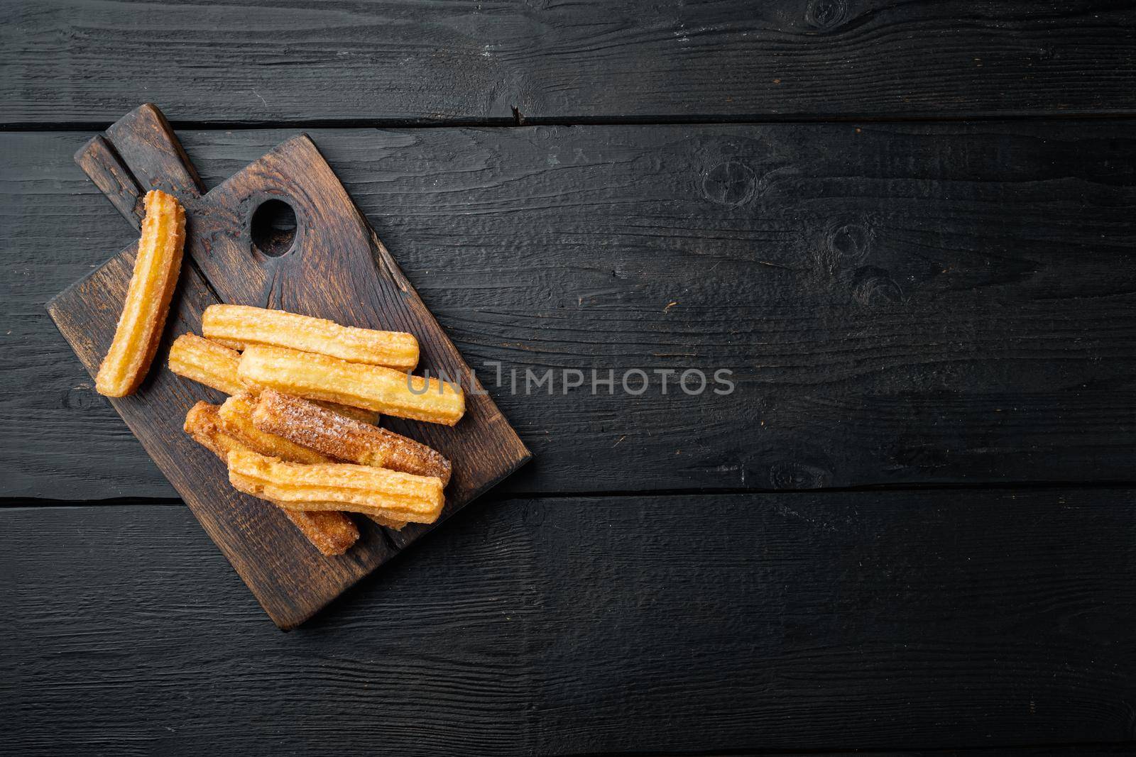 Churros sprinkled with powdered sugar set, on black wooden table background, top view flat lay with space for text, copyspace
