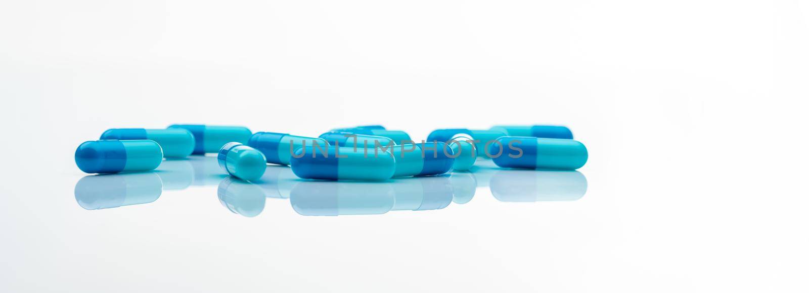 Blue antibiotic capsule pills spread on white background. Antibiotic drug resistance. Pharmaceutical industry. Healthcare and medicine concept. Health budget concept. Capsule manufacturing industry. by Fahroni