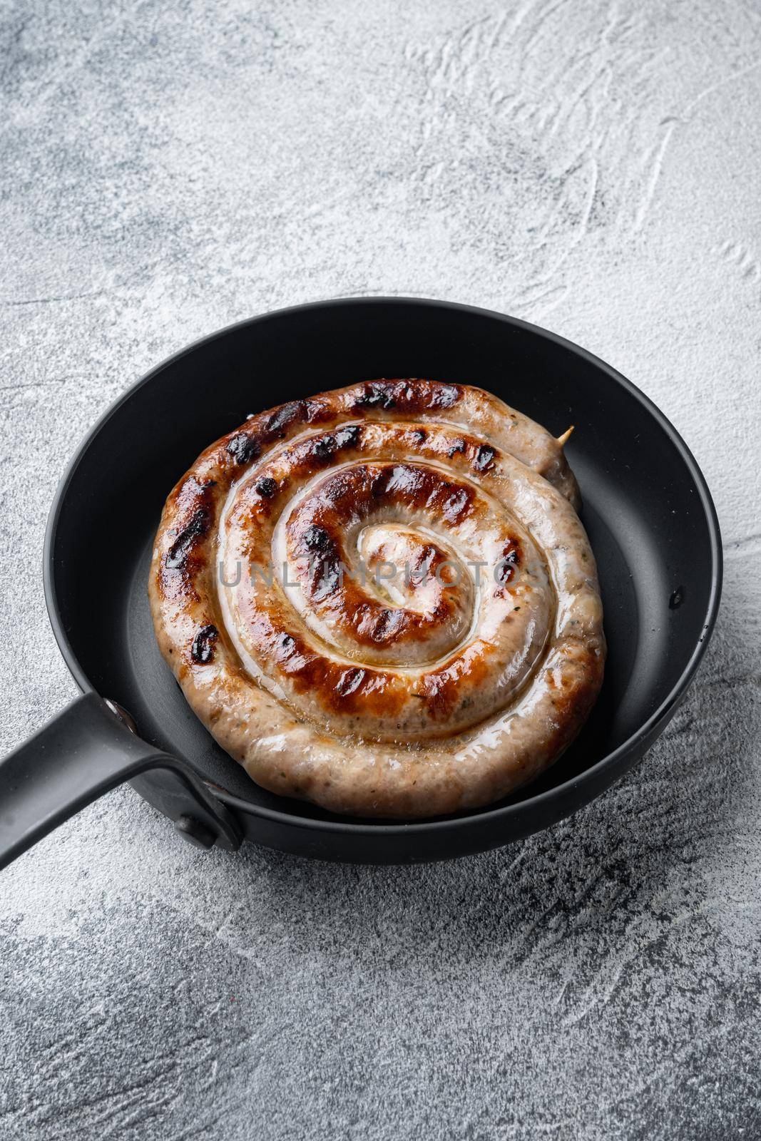 Homemade Spiral grilled sausage set in cast iron frying pan, on gray background