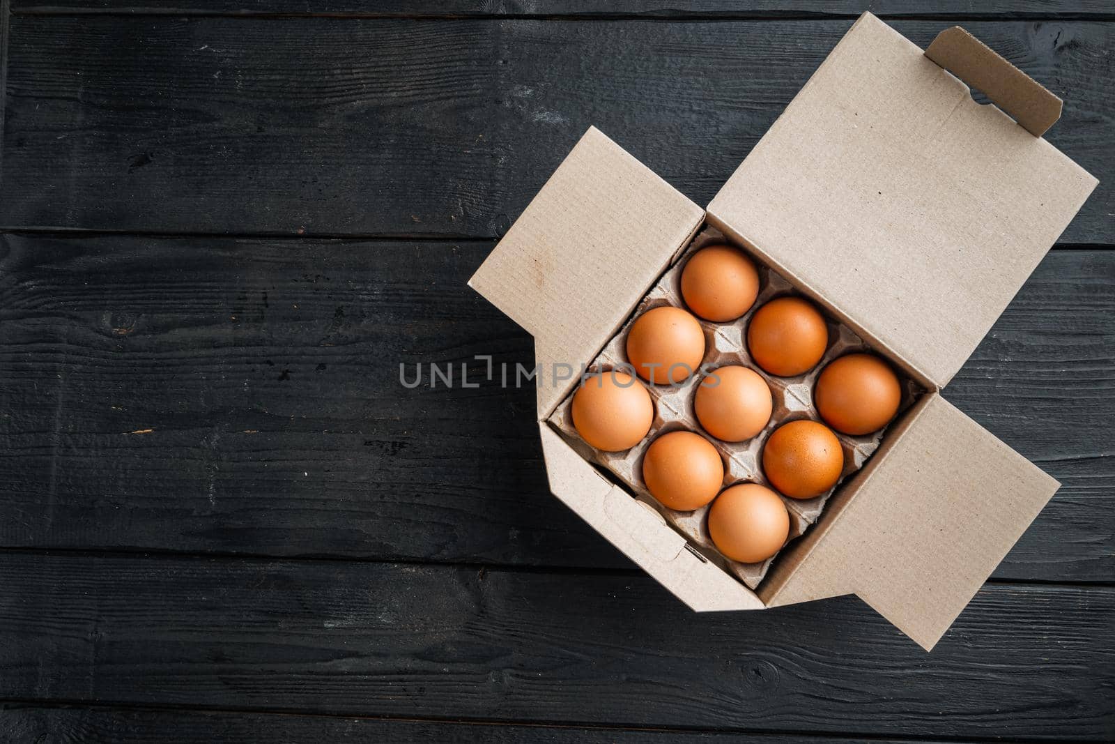 Chicken eggs in an egg box tray set, on black wooden table background, top view flat lay , with space for text copyspace