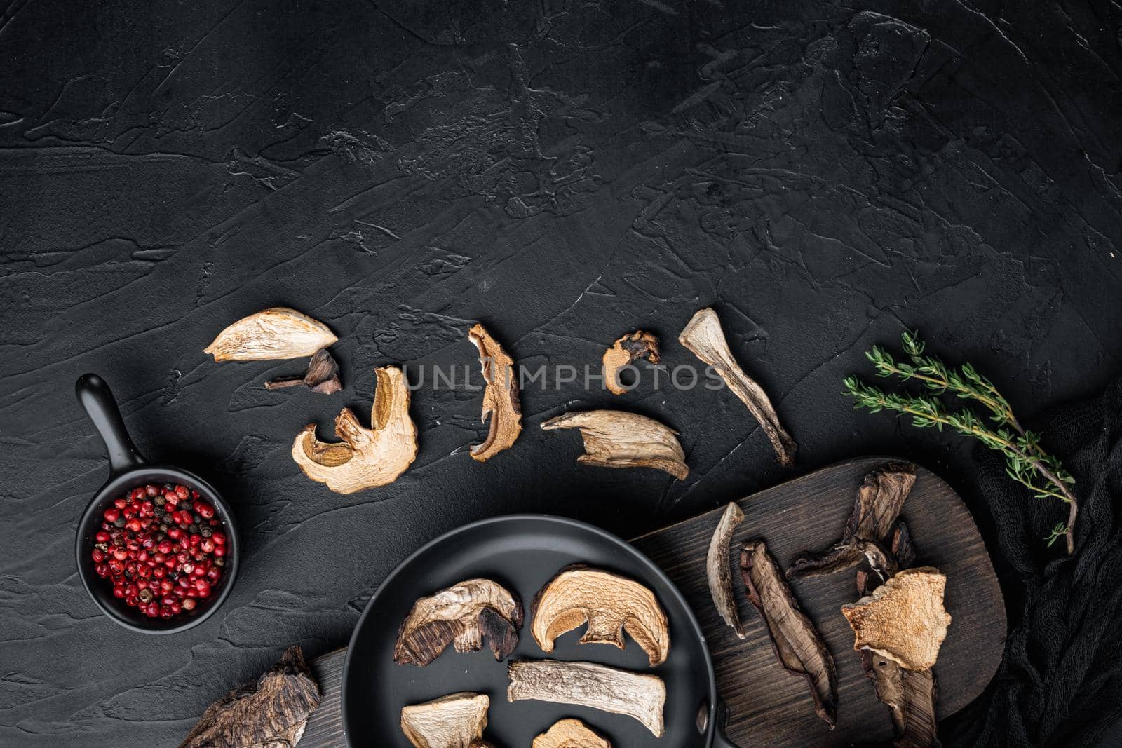 Dried wild mushrooms set in cast iron frying pan, on black background, top view flat lay , with space for text copyspace