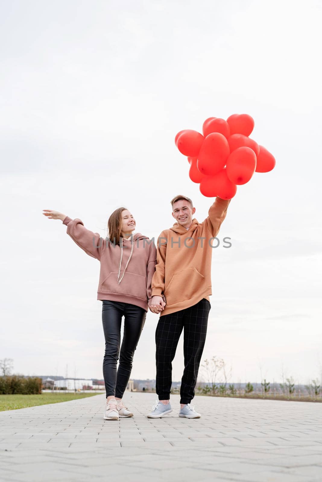 Valentines Day. Young loving couple hugging and holding red heart shaped balloons outdoors