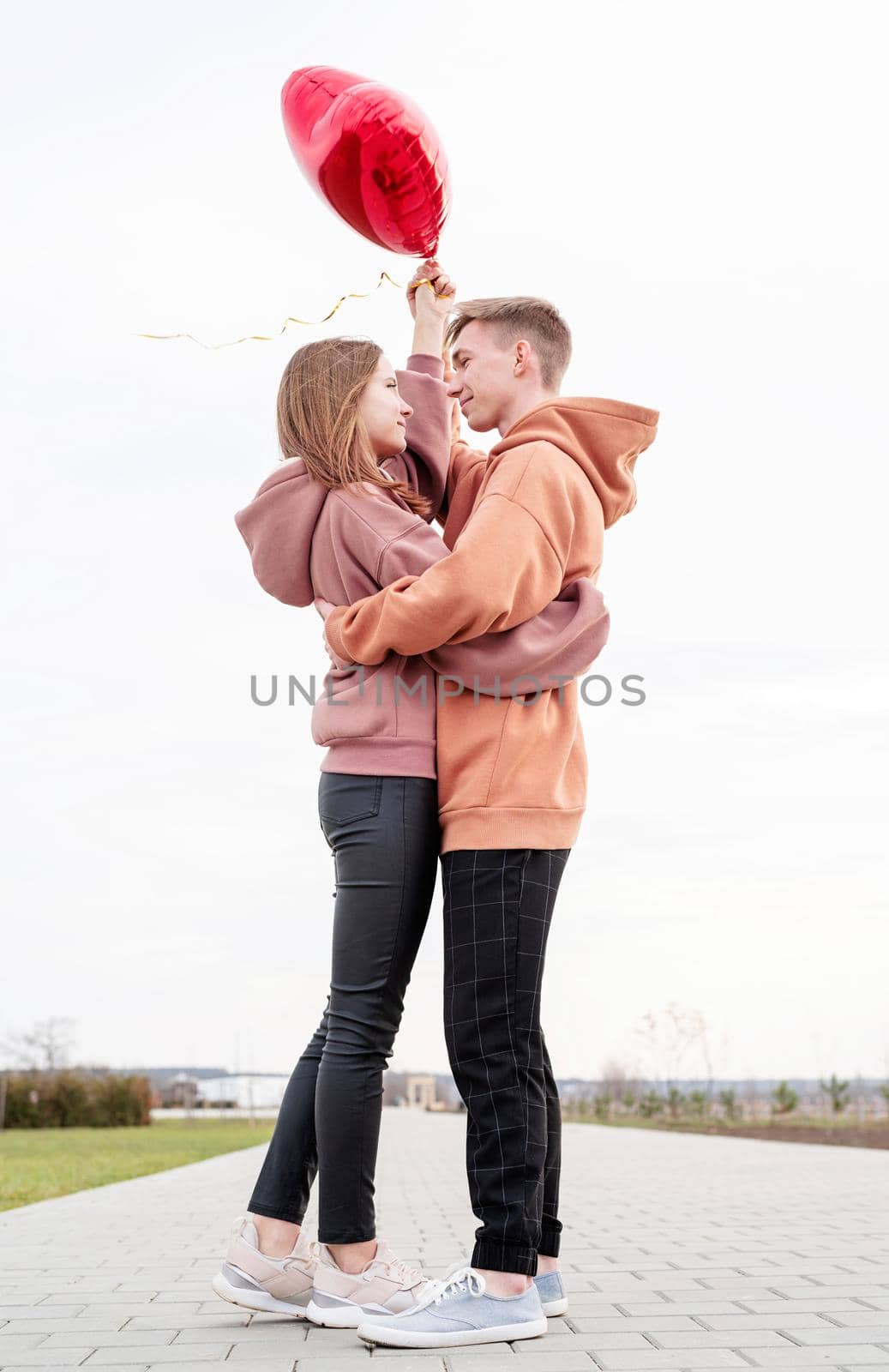 Valentines Day. Young loving couple hugging and holding red heart shaped balloons outdoors