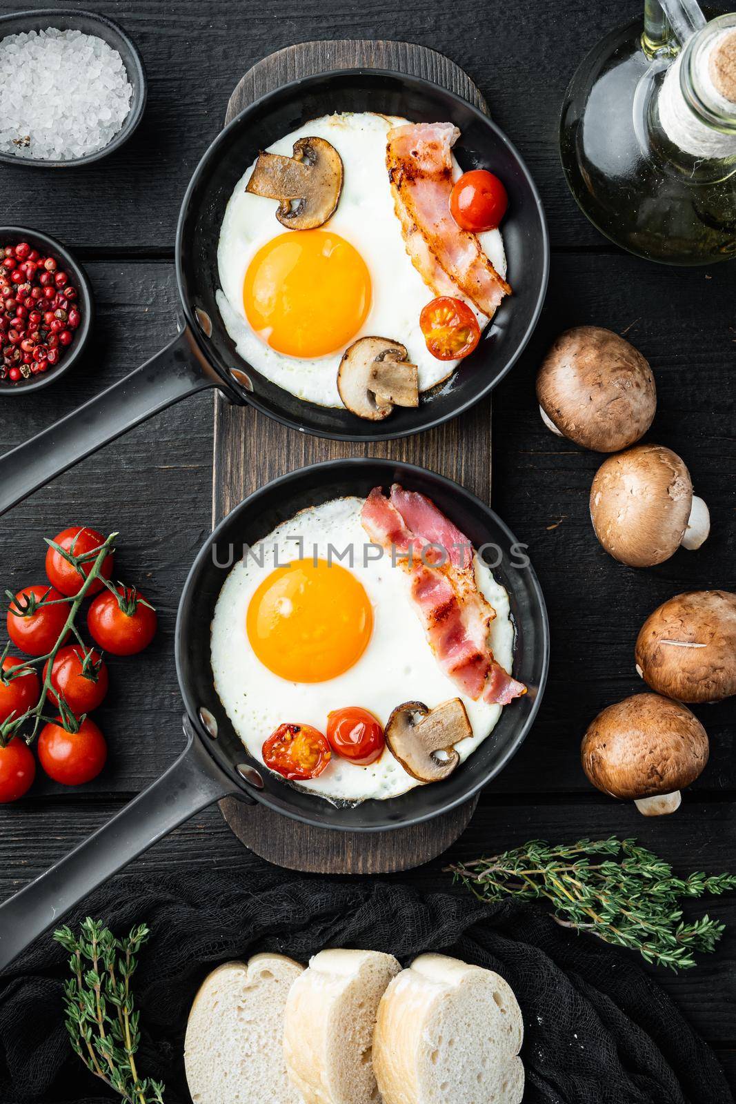 Scrambled eggs in frying pan with pork lard, bread and green feather in cast iron frying pan, on black wooden table background, top view flat lay