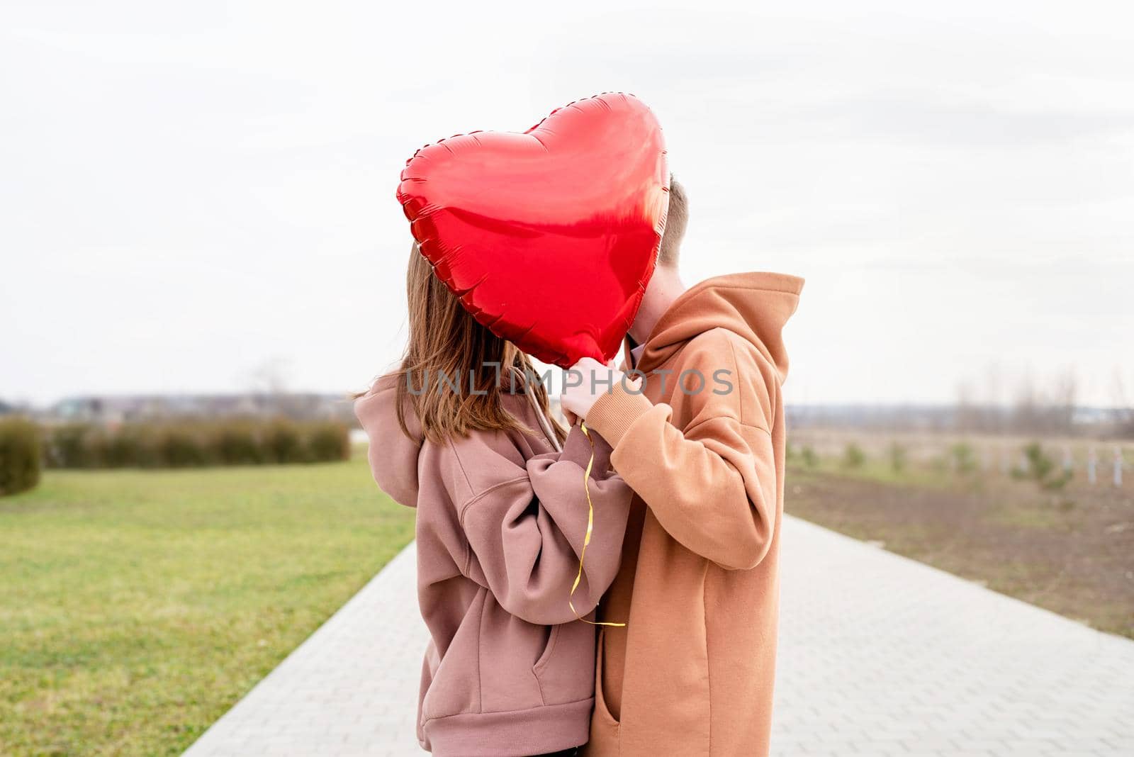 Valentines Day. Young loving couple hugging and holding red heart shaped balloon outdoors