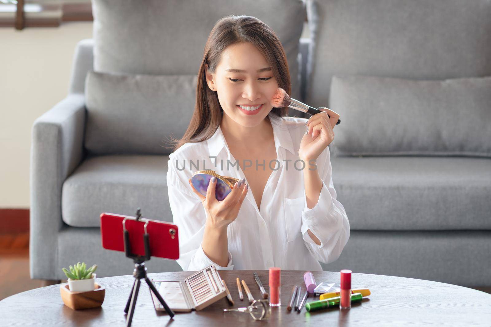 Asian female beauty influencer making a video tutorial for her beauty channel on cosmetics during stay safe at home