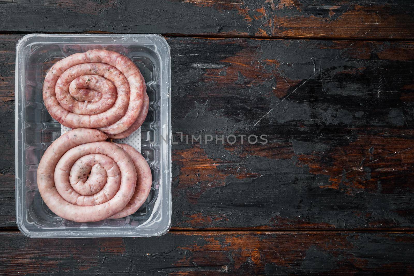 Traditional raw spiral pork sausages set, on old dark wooden table background, in plastic pack, top view flat lay , with space for text copyspace