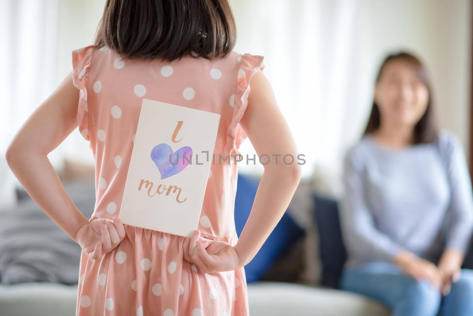 Asian cute girl hide handmade greeting card with i love mom word to give surprising her mother at home